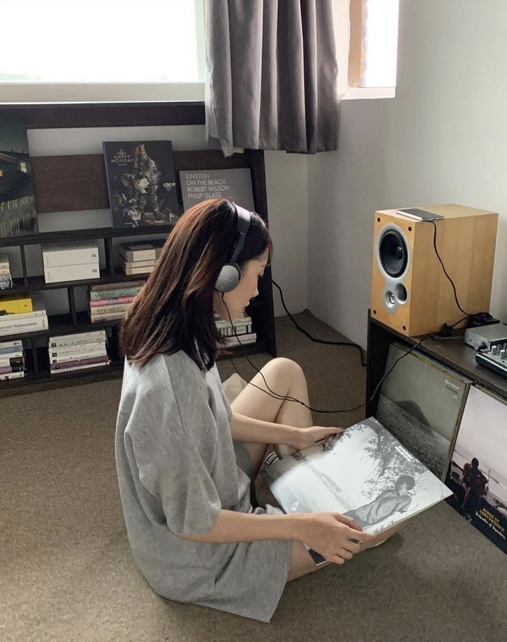 A woman in a grey T-shirt wearing headphones and looking at an LP record