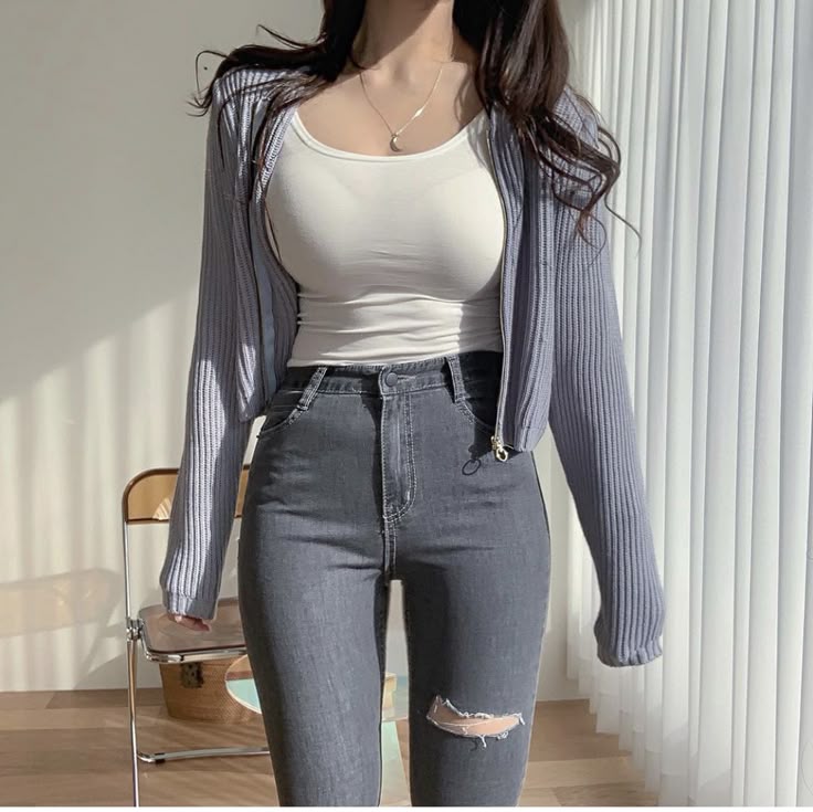 Woman wearing white sleeveless, cropped zip-up, and gray ripped skinny jeans