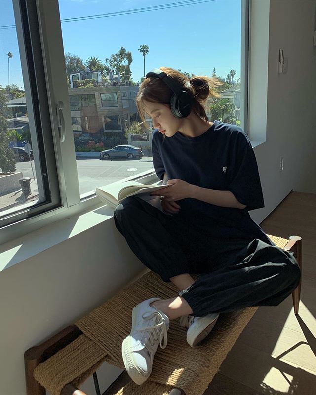 Woman reading book by window with headphones on in a cozy mood