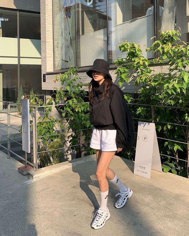 Woman wearing black bucket hat, white shorts and sneakers in a street fashion look