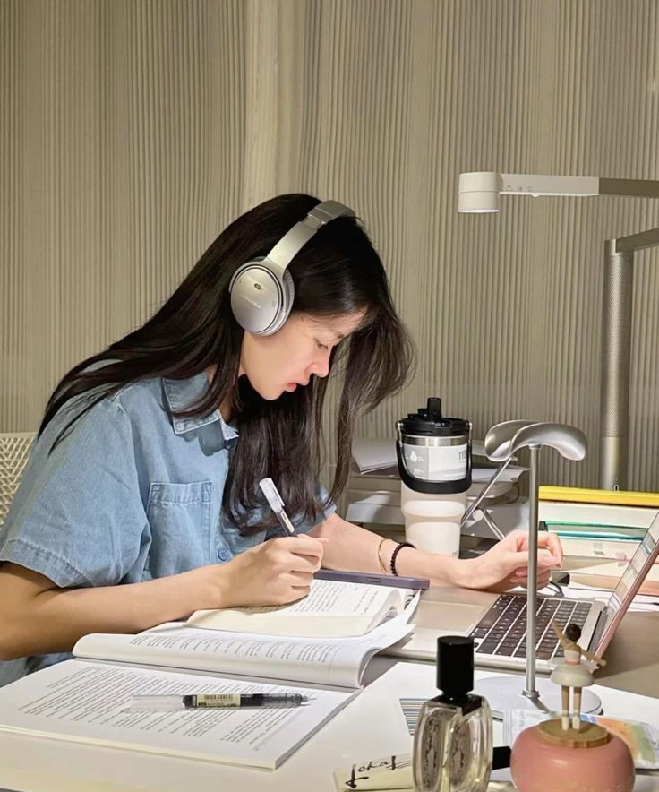 Woman studying at desk with headphones on, focused mood
