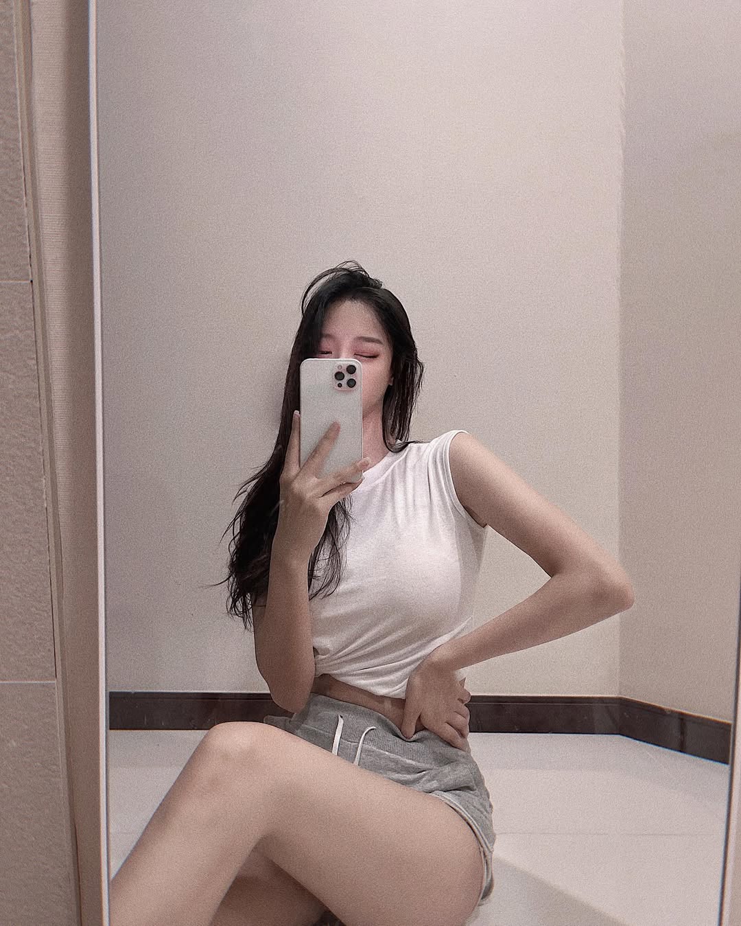 Woman in white crop top and gray jogger shorts taking a mirror selfie