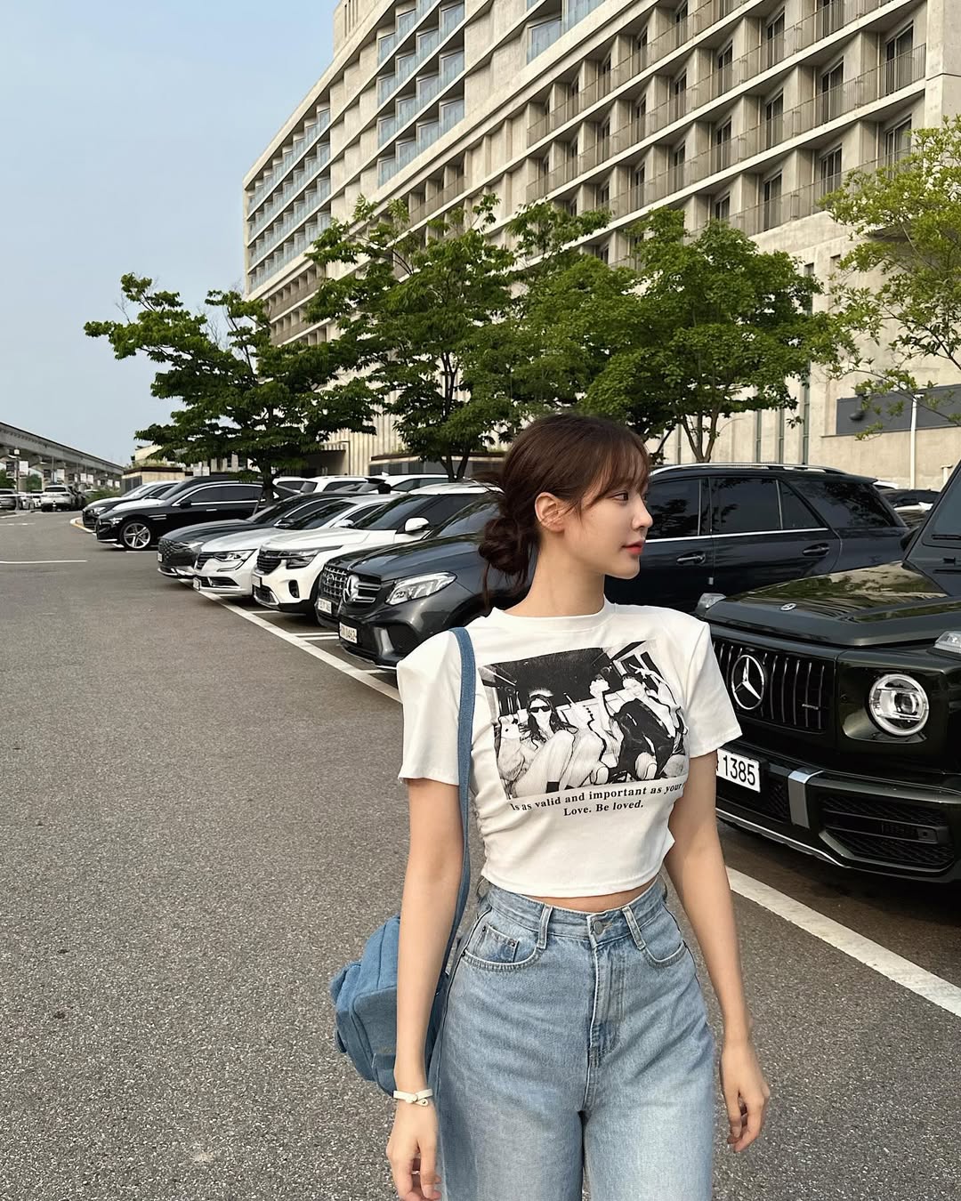 Woman in graphic tee, light denim, and backpack standing on street.