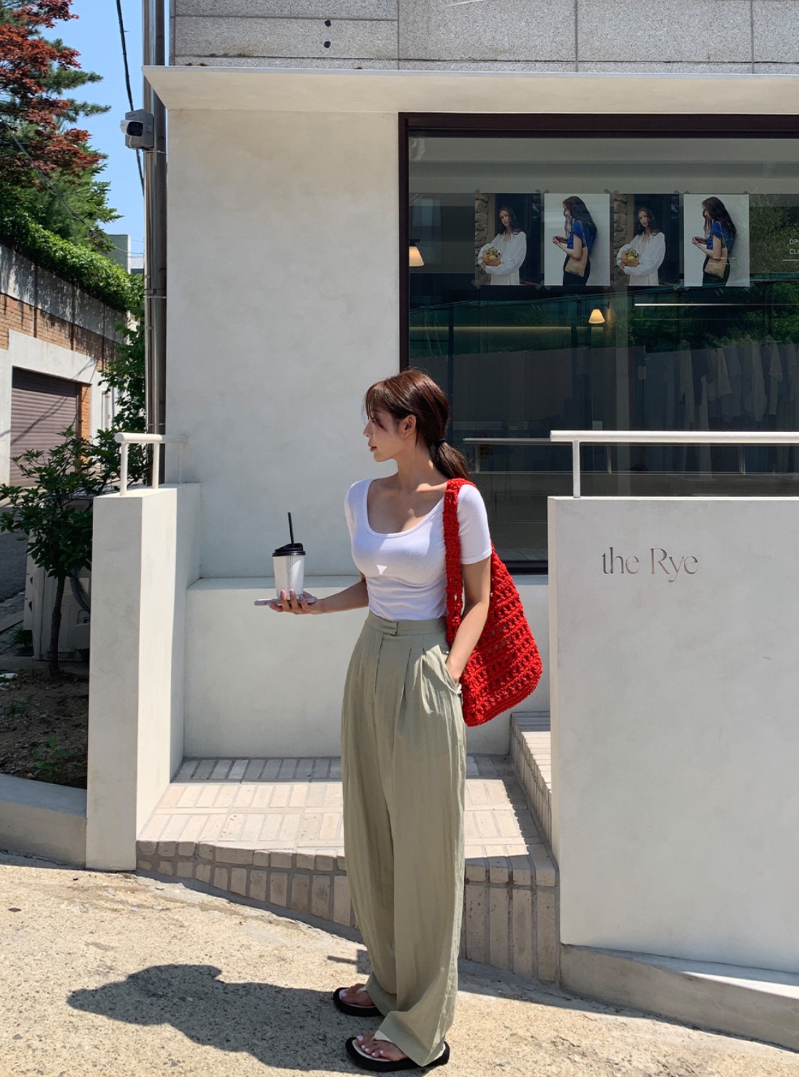 Woman wearing square-neck top, linen pants, and red knit bag