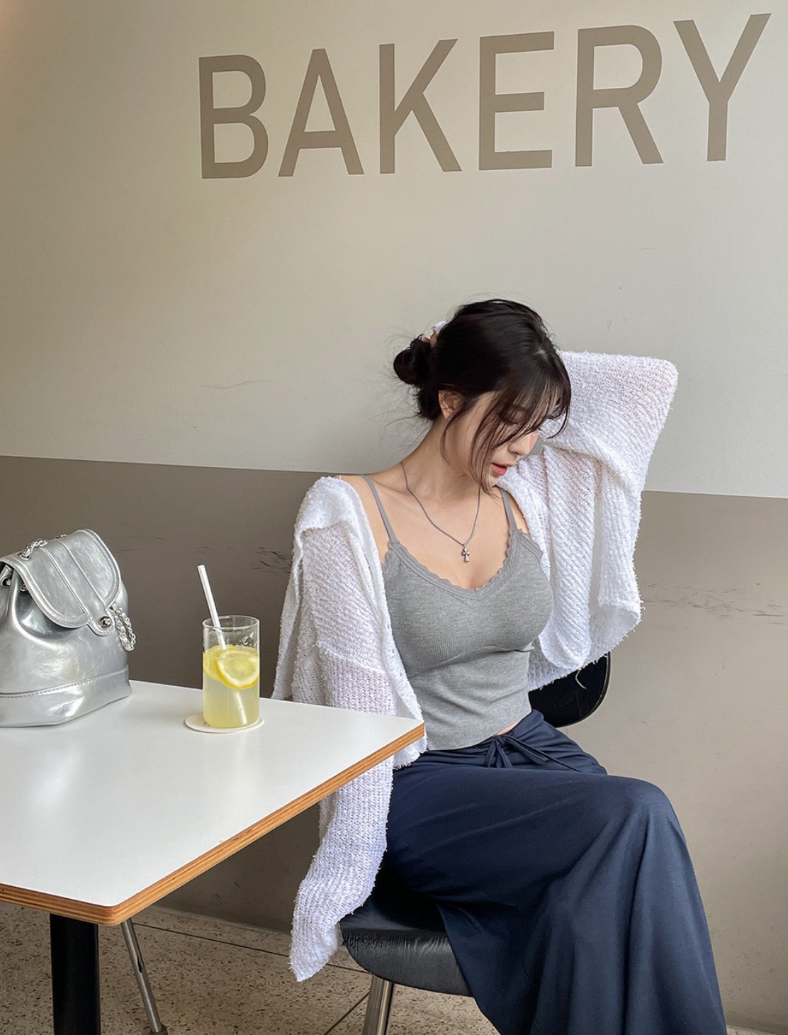 Woman wearing grey lace cami, navy skirt, white cardigan, and silver bag.