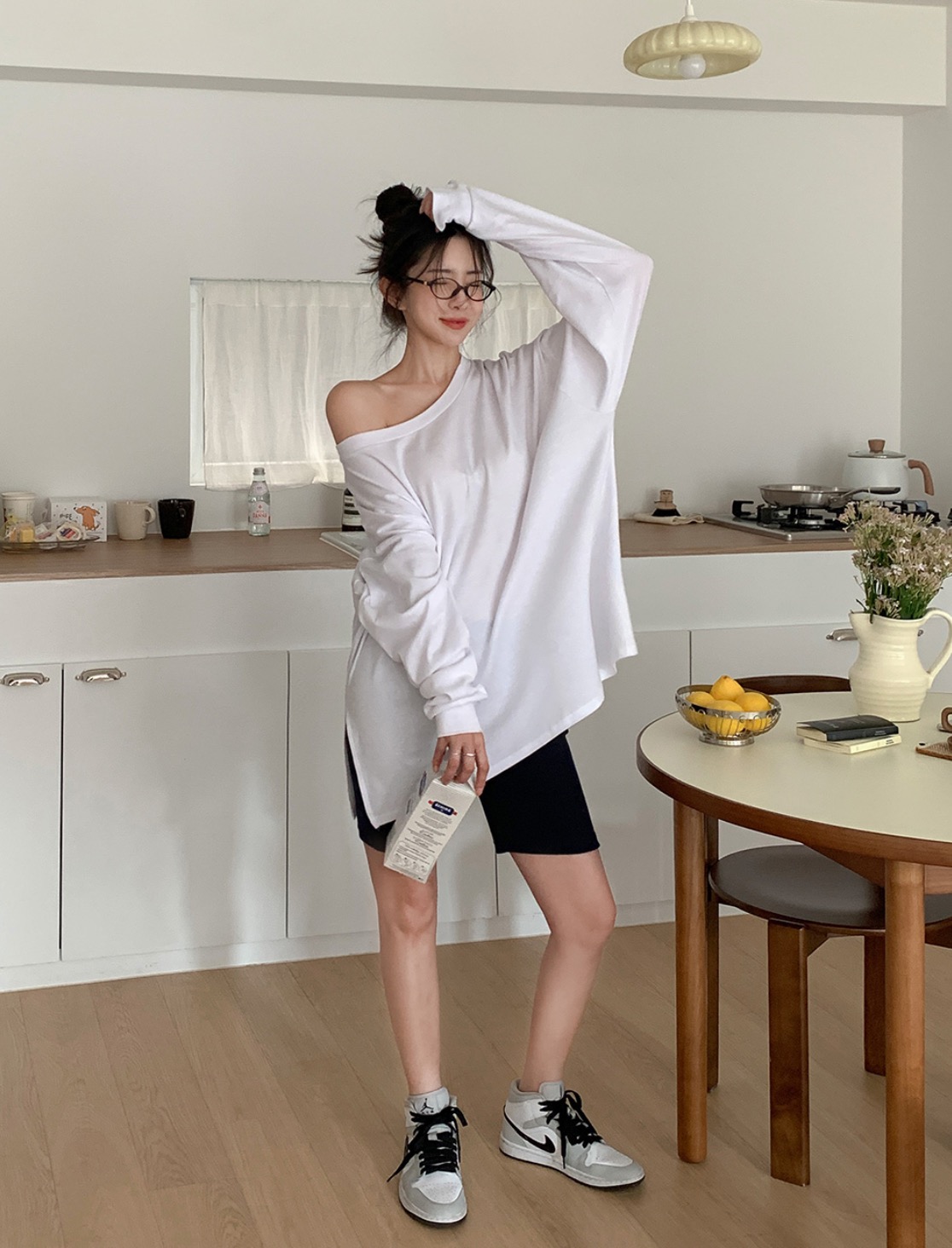 Woman in white oversized t-shirt and biker shorts posing in a kitchen.