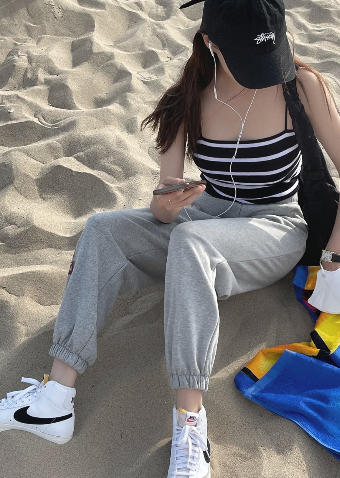 Woman wearing stripe crop top, jogger pants, and Nike sneakers on beach.