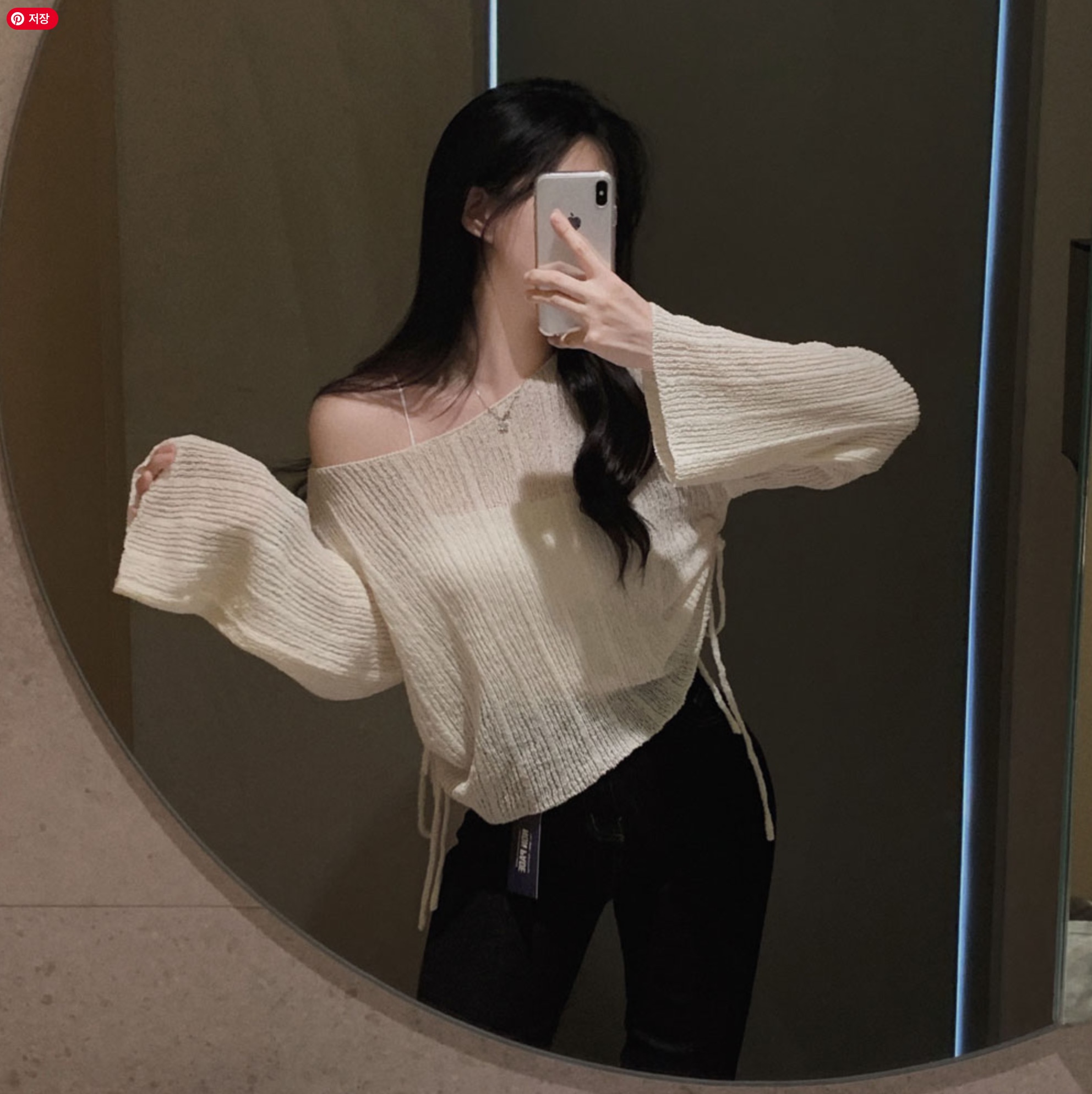 Woman wearing off-shoulder knit and black pants in mirror selfie.