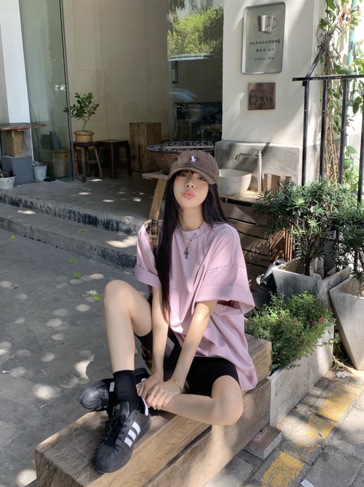 Woman in pink t-shirt and cap sitting casually in streetwear outfit