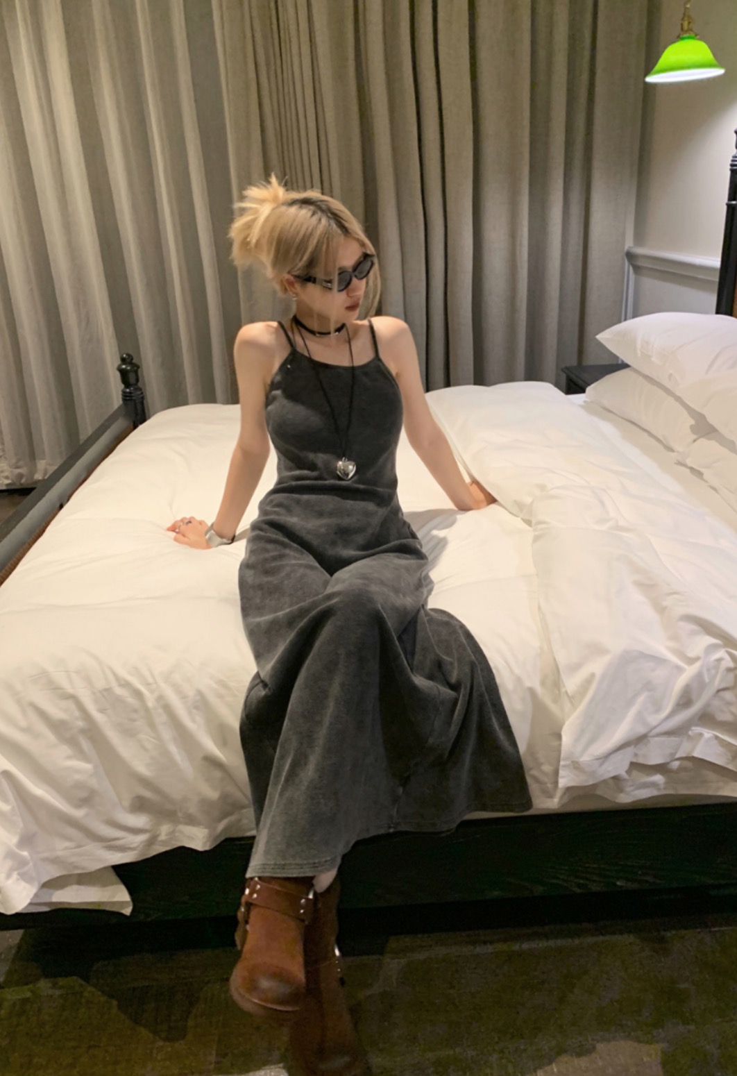 Chic woman in velvet long dress sitting on bed with boots