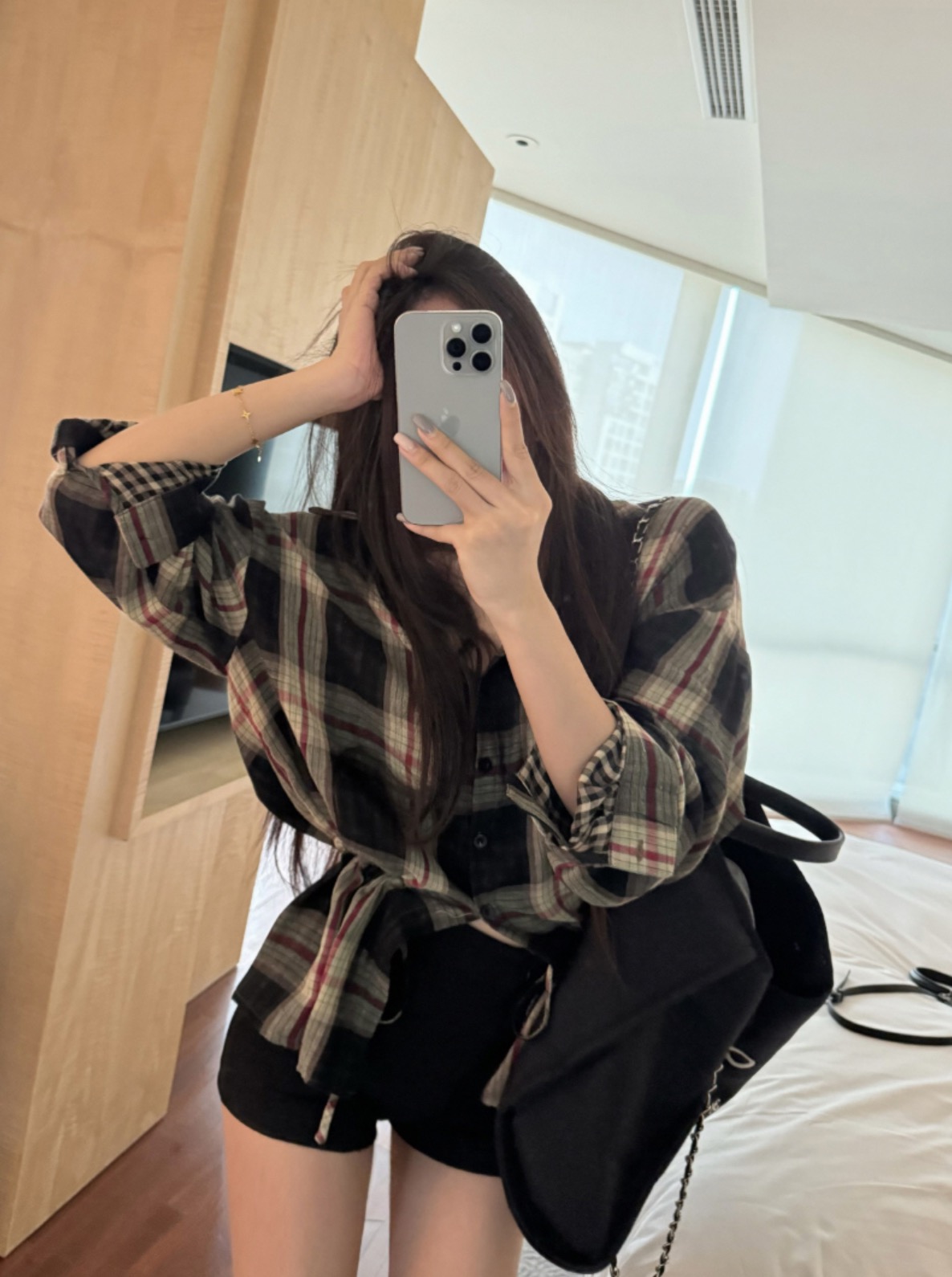 Woman in check shirt taking mirror selfie with black shorts and backpack