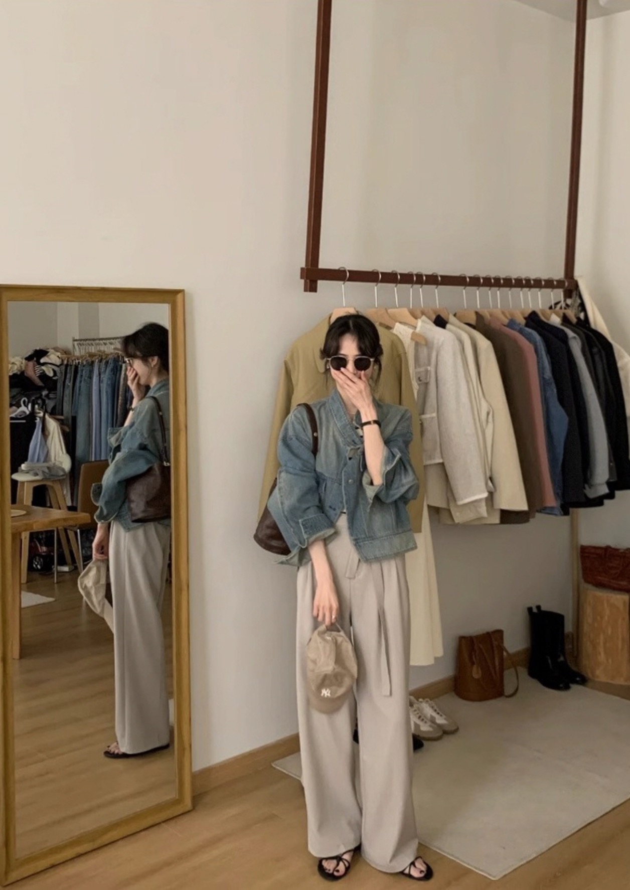 Woman in denim jacket and wide beige pants holding a cap